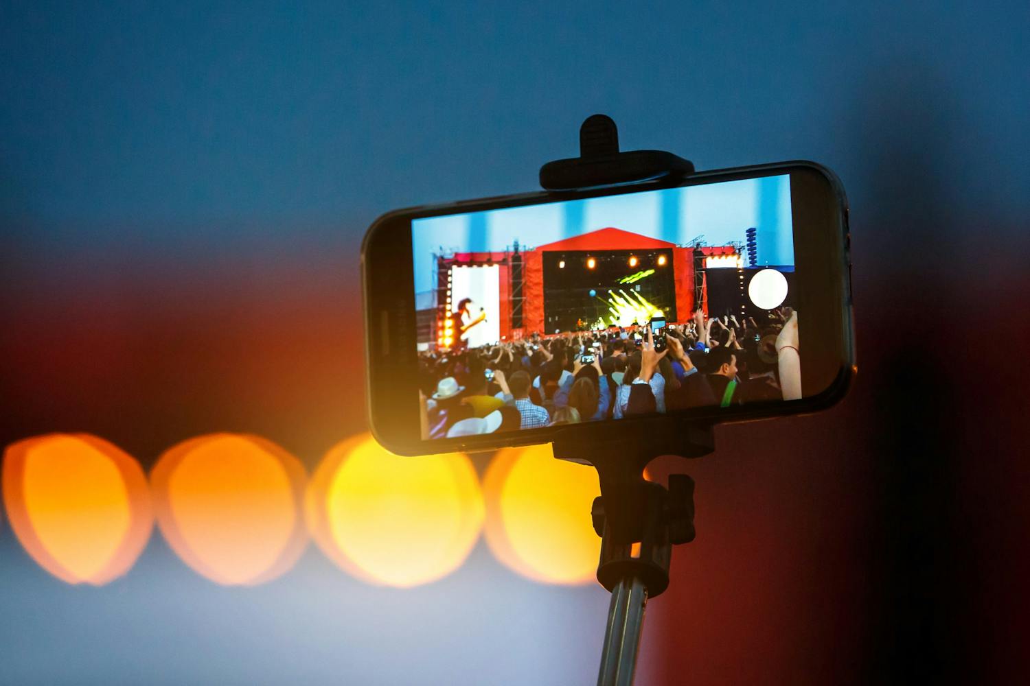 En person skyder et foto med en selfiestang til en koncert